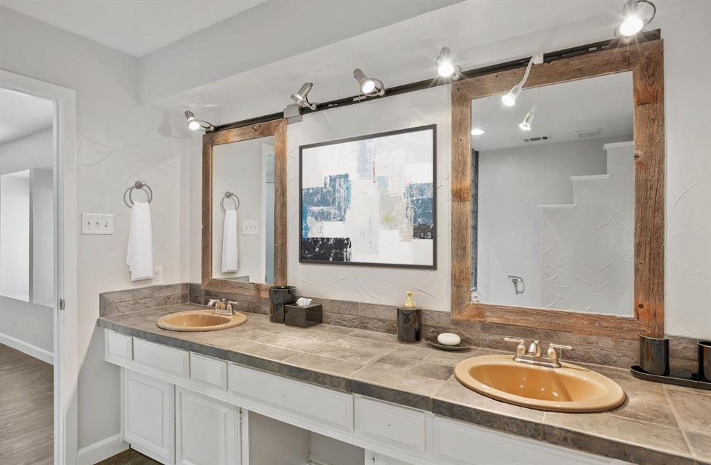 Dual-sink vanity featuring tile countertops, white cabinetry, integrated wood-framed mirrors, and track lighting
