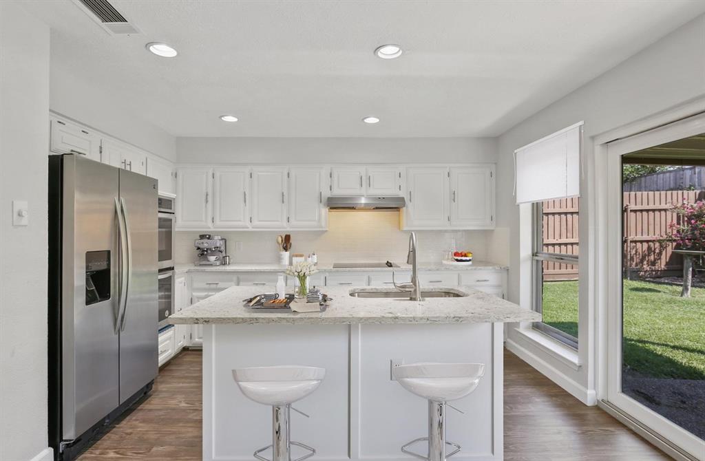 Kitchen featuring a center island with a stone countertop, white shaker-style cabinetry, stainless steel appliances, recessed lighting, and wood-finish flooring