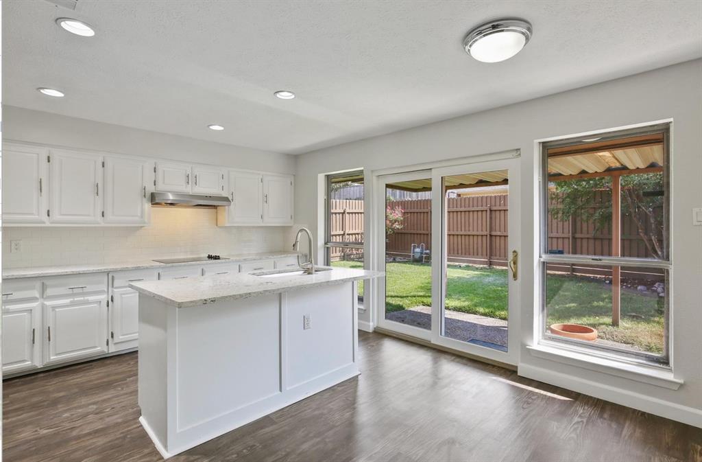 Kitchen featuring white cabinetry, stone-surface countertops, central island, wood-finish flooring, and sliding glass door access to a fenced rear yard