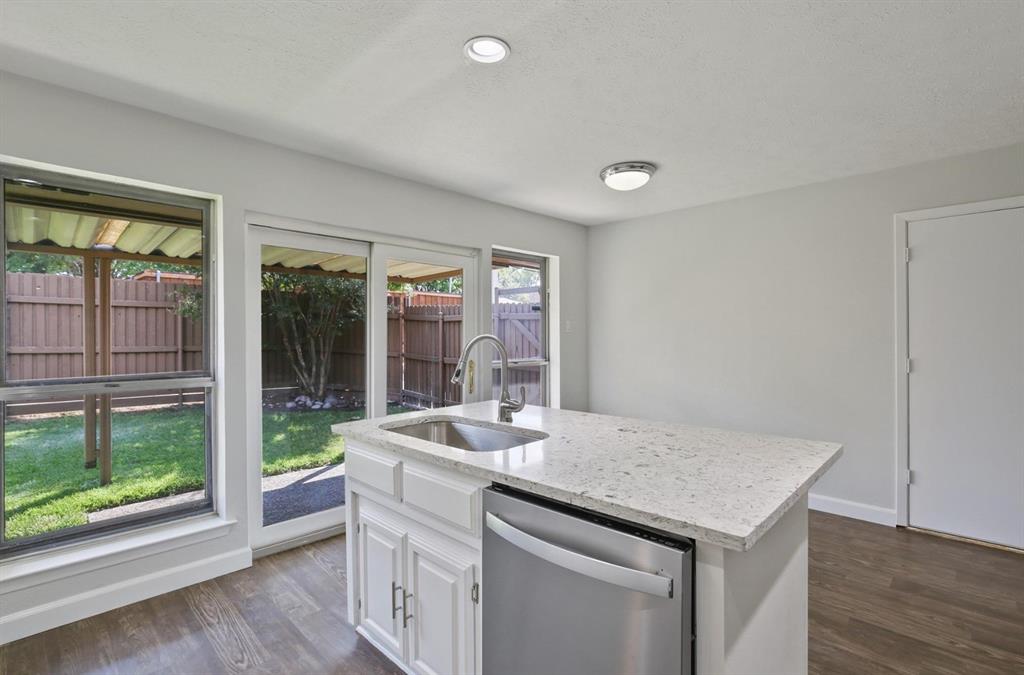 Kitchen island featuring a stone-composite countertop, stainless steel undermount sink with a gooseneck faucet, built-in stainless steel dishwasher, white cabinetry, and wood-finish flooring