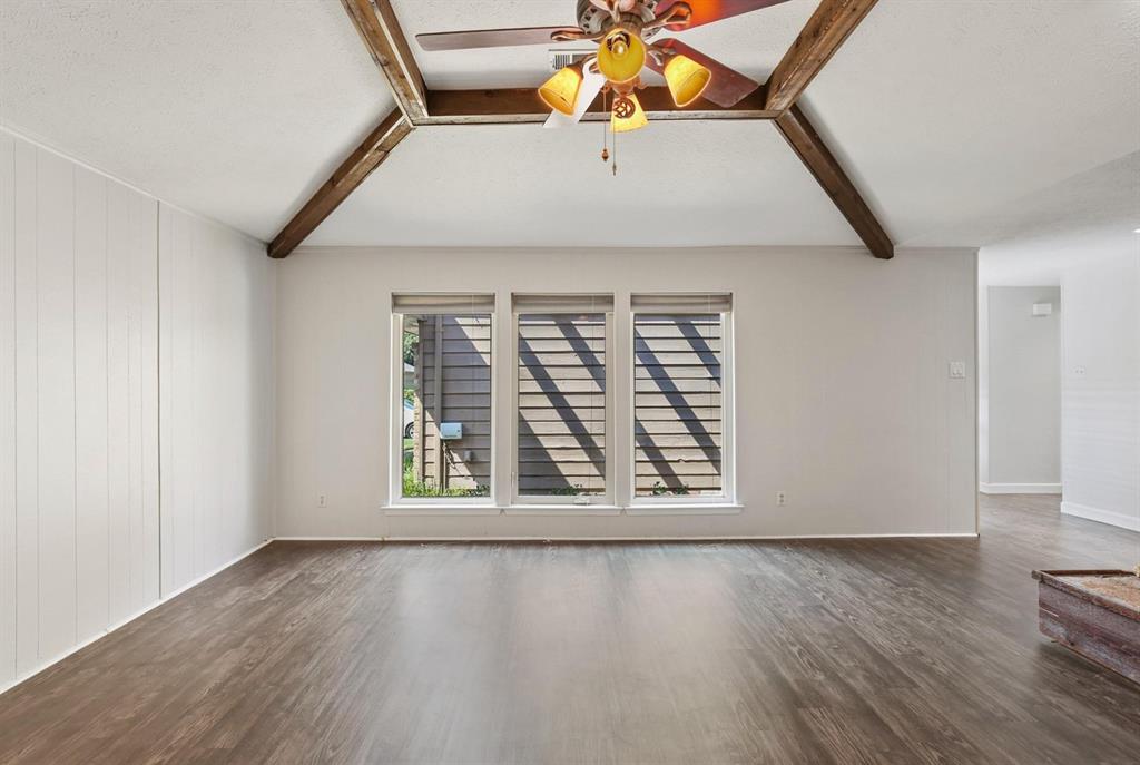 Vaulted ceiling featuring exposed wood beams, triple window arrangement, and wood-finish flooring