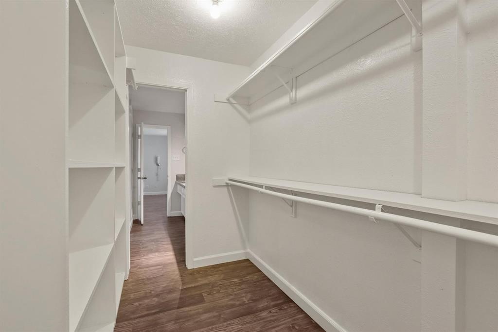 Walk-in closet featuring built-in vertical shelving, dual-tier hanging rods, and wood-finish flooring