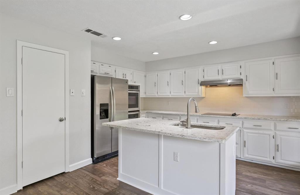 Kitchen featuring white cabinetry, stone-surface countertops, central island with an integrated sink, stainless steel appliances, and wood-finish flooring