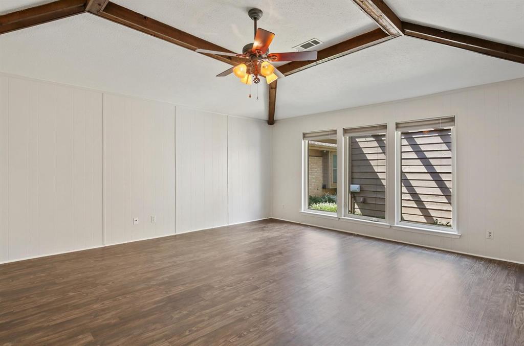 Vaulted ceilings featuring exposed wood-finish beams, wood-finish flooring, and a central ceiling fan with integrated lighting, complemented by a trio of windows