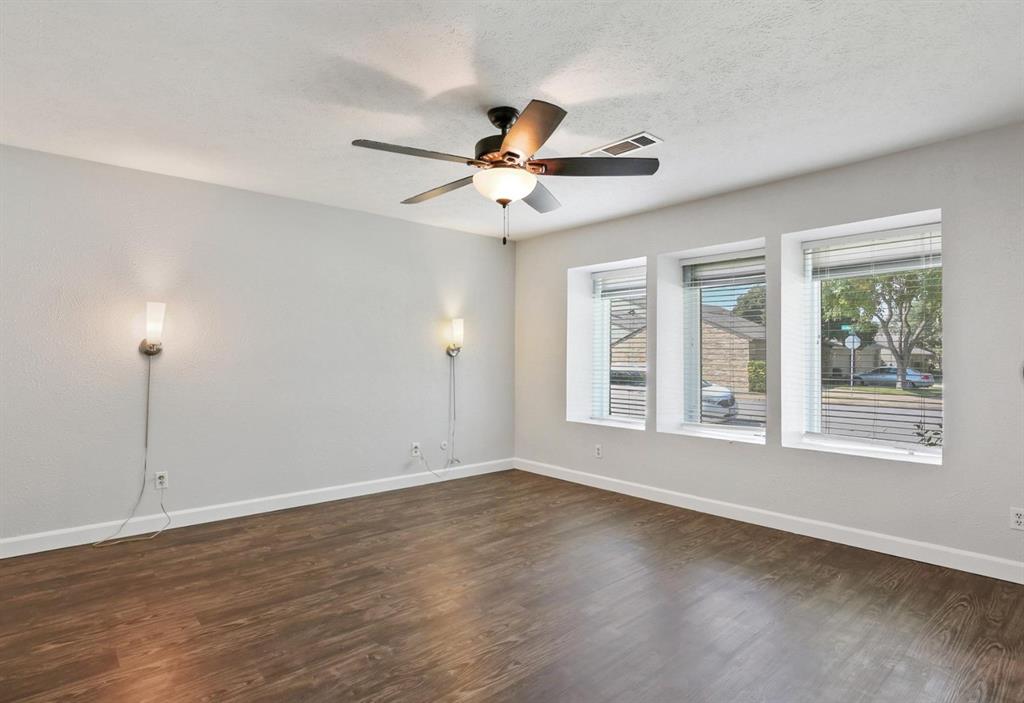 Wood-finish flooring, recessed window bays with natural lighting, dual wall-mounted light fixtures, and a central ceiling fan