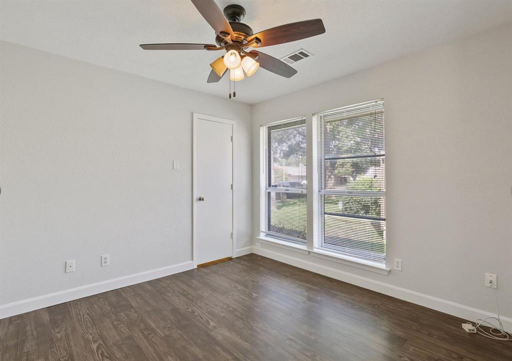 Neutral-toned interior room featuring wood-finish flooring, dual windows with integrated blinds, and a multi-blade ceiling fan with a triple-light fixture