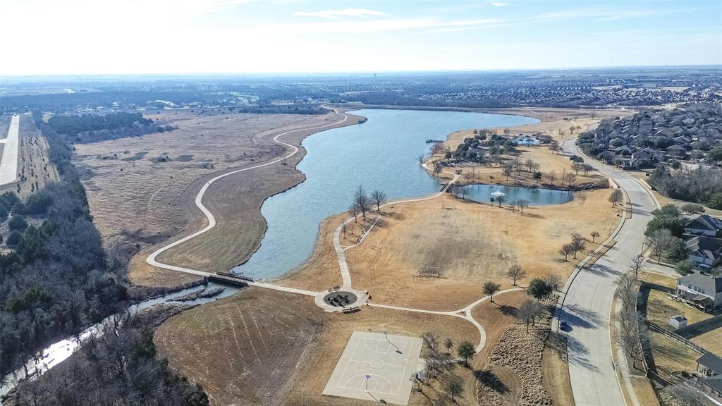 Aerial perspective featuring a large lake, paved walking paths, a basketball court, and mature trees