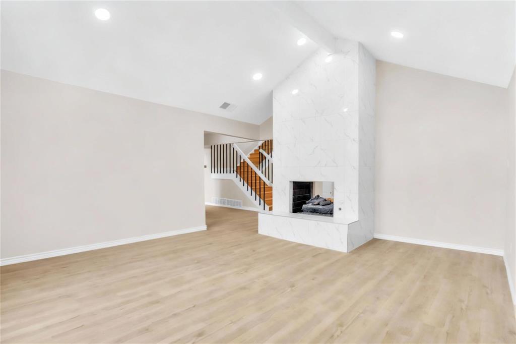 Vaulted ceilings, wood-finish flooring, recessed lighting, and a full-height fireplace surround featuring a stone-pattern finish with a matching raised hearth