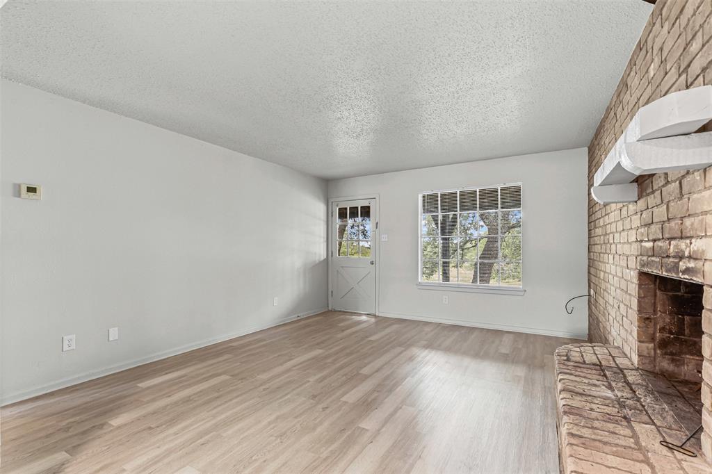 Unfurnished living room featuring a textured ceiling, light wood-style flooring, and a brick fireplace