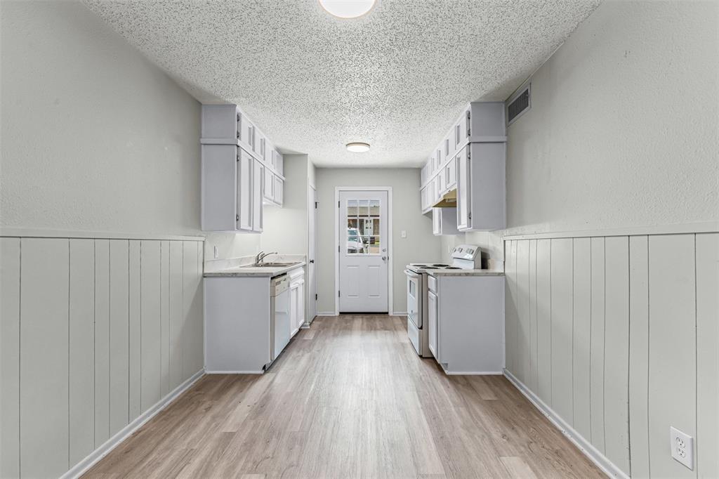 Kitchen with white appliances, light wood-type flooring, a textured ceiling, light countertops, and a wainscoted wall