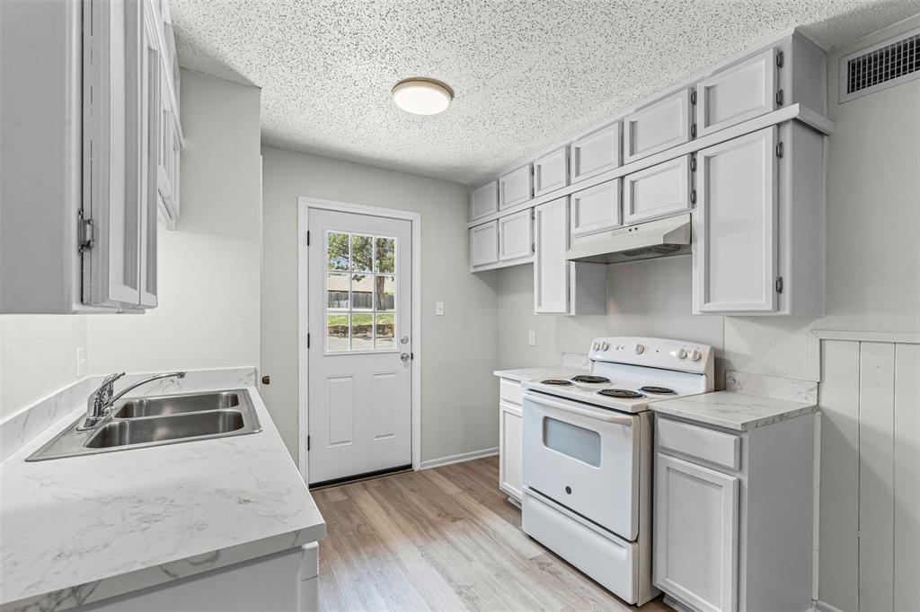 Kitchen featuring white electric range, a textured ceiling, light countertops, under cabinet range hood, and light wood-style flooring