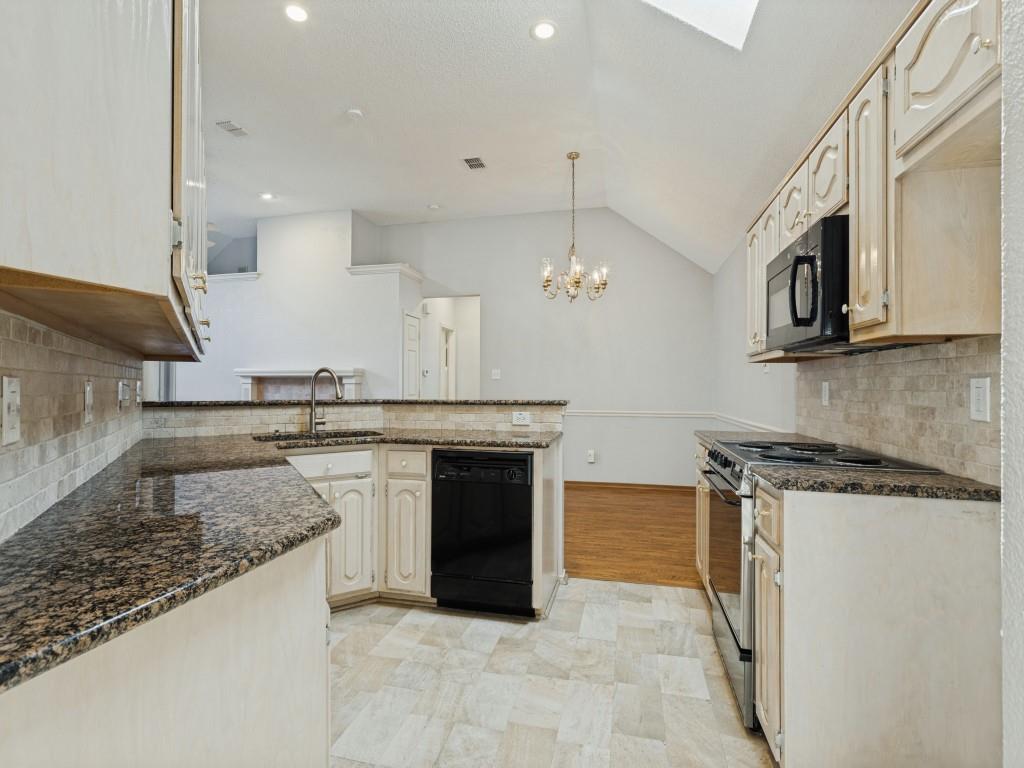 Kitchen featuring light-toned cabinetry, granite countertops, tiled backsplash, built-in black appliances, and a vaulted ceiling with a skylight Kitchen featuring light-toned cabinetry, granite countertops, tiled backsplash, built-in black appliances, and a vaulted ceiling with a skylight