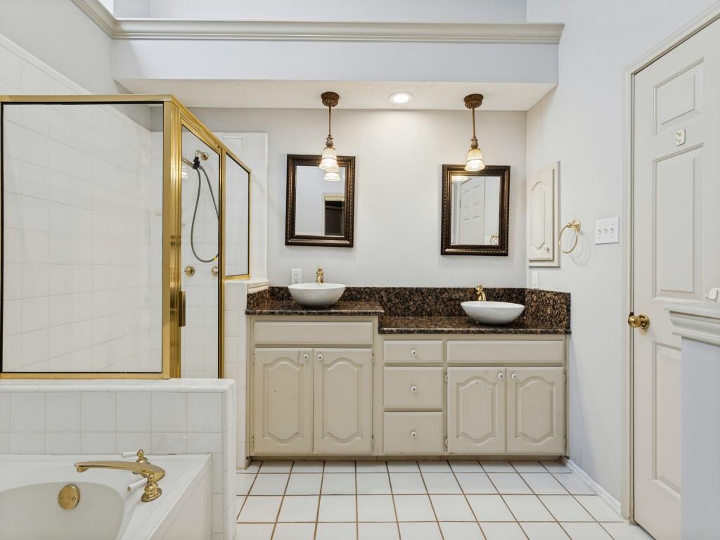 Dual-vanity cabinetry with dark stone countertops, vessel sinks, pendant lighting, walk-in shower with metal-finish frame, and tile flooring