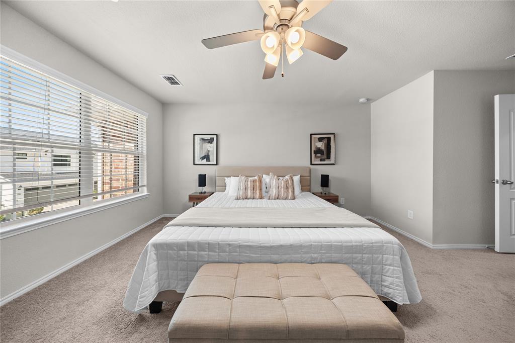 Neutral-toned room featuring wall-to-wall carpeting, large windows with horizontal blinds, and a central ceiling fan with multi-light fixture