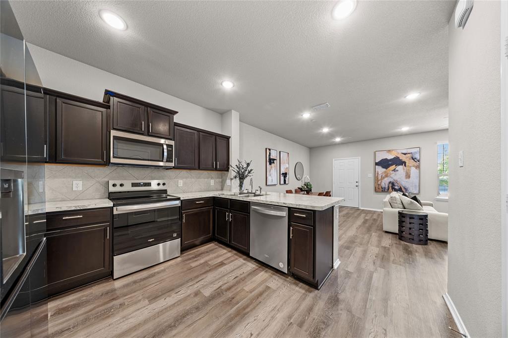 Kitchen featuring dark wood cabinetry, stainless steel appliances, neutral stone-finish countertops, recessed ceiling lighting, and wood-finish flooring