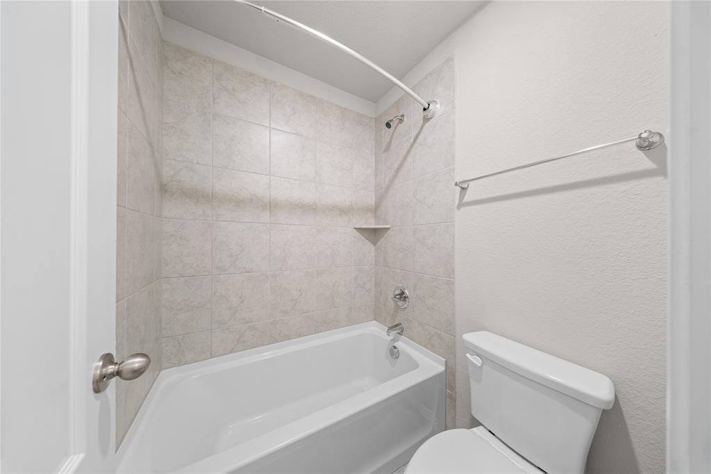 Bathroom featuring a white acrylic bathtub, neutral-toned wall tile surround, built-in corner soap ledge, chrome finish plumbing fixtures, and a wall-mounted towel bar