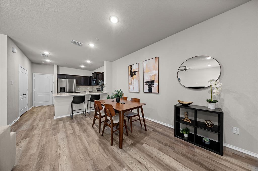 Open-concept kitchen featuring dark wood cabinetry, stainless steel appliances, and a quartz breakfast bar with pendant lighting, complemented by wood-finish flooring throughout