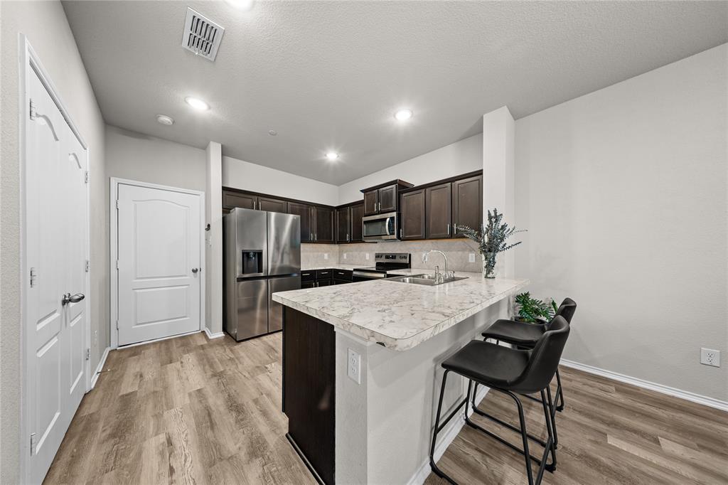 Kitchen featuring dark-finish cabinetry, stone-patterned countertops, stainless steel appliances, and wood-finish flooring