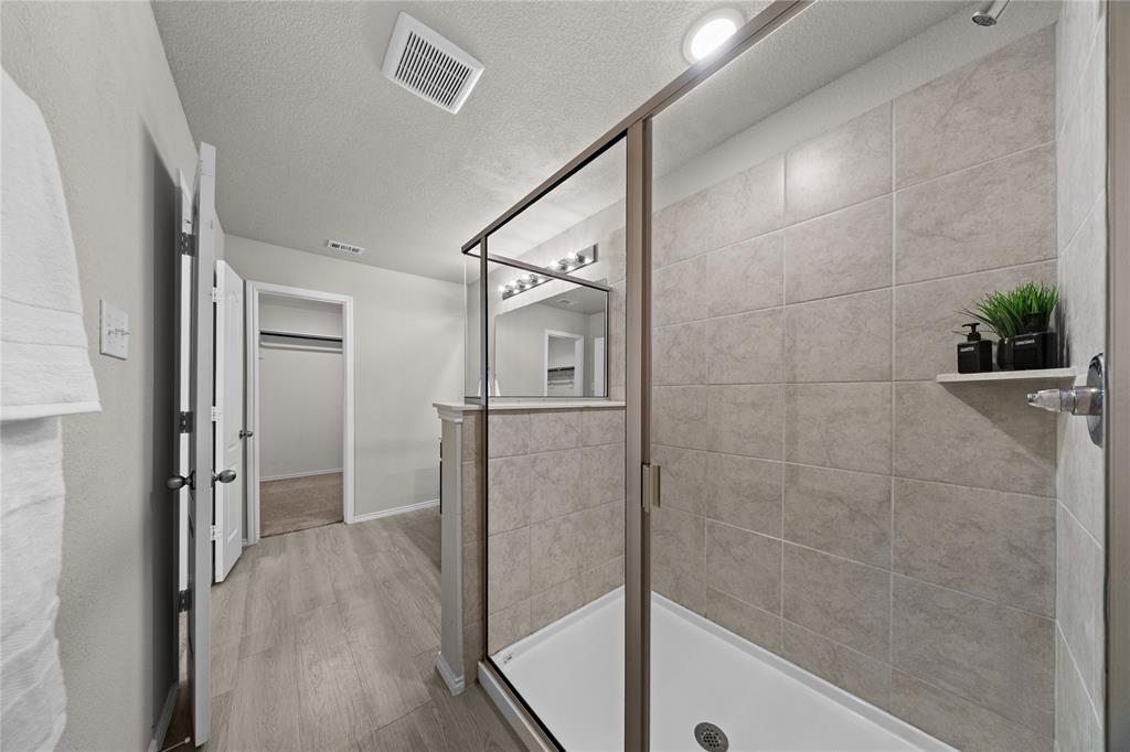 Walk-in shower with floor-to-ceiling tile surround and metal-framed glass enclosure, wood-finish flooring, and recessed ceiling lighting