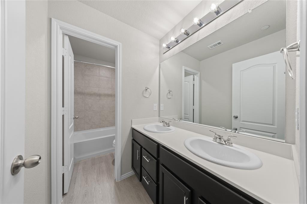 Double vanity featuring a light-toned countertop, dual integrated sinks, dark-finish cabinetry, and a full-width mirror with integrated lighting