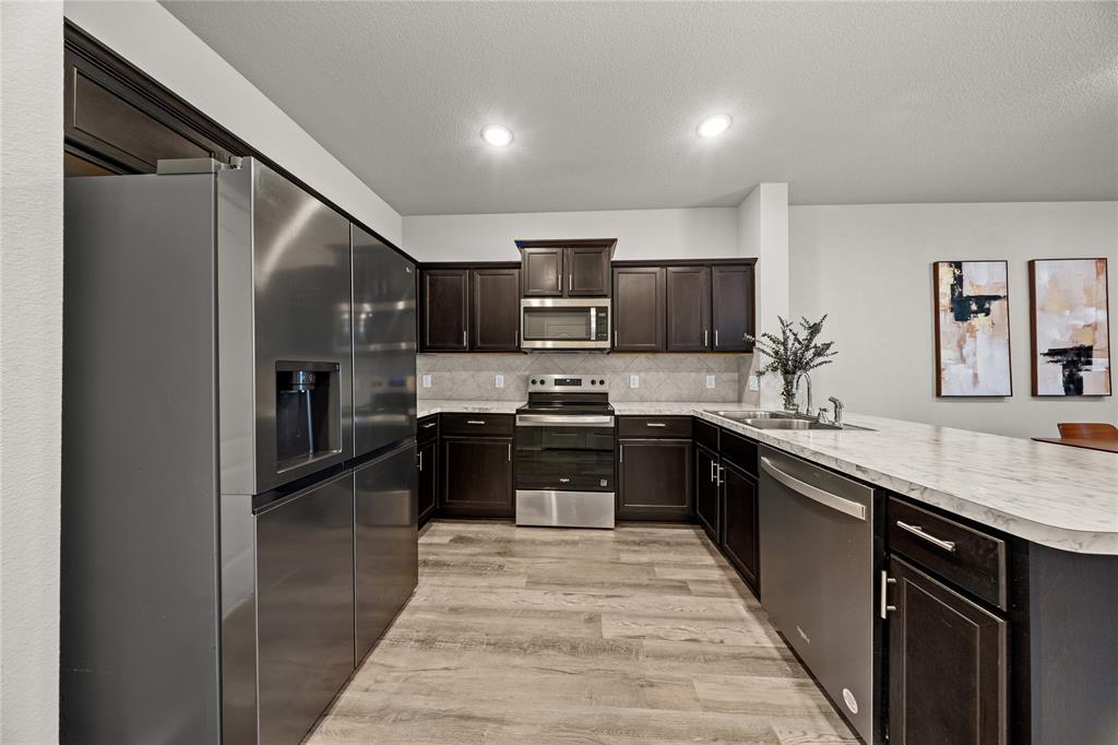 Kitchen featuring dark wood cabinetry, stainless steel appliances, stone-patterned countertops, wood-finish flooring, and recessed ceiling lighting
