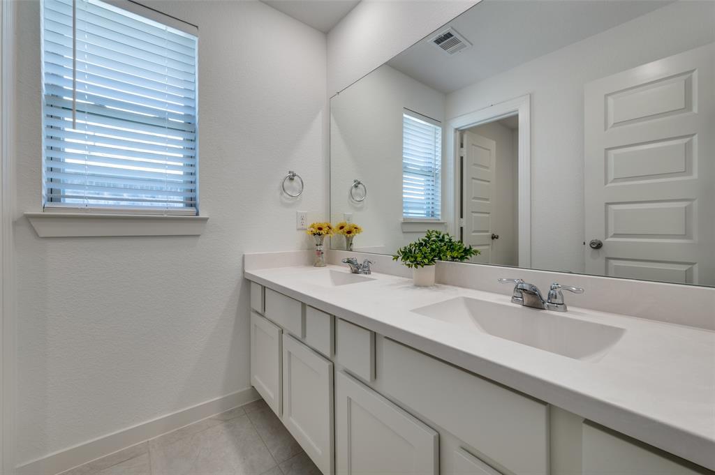 Full bathroom with double vanity, a textured wall, and light tile patterned floors