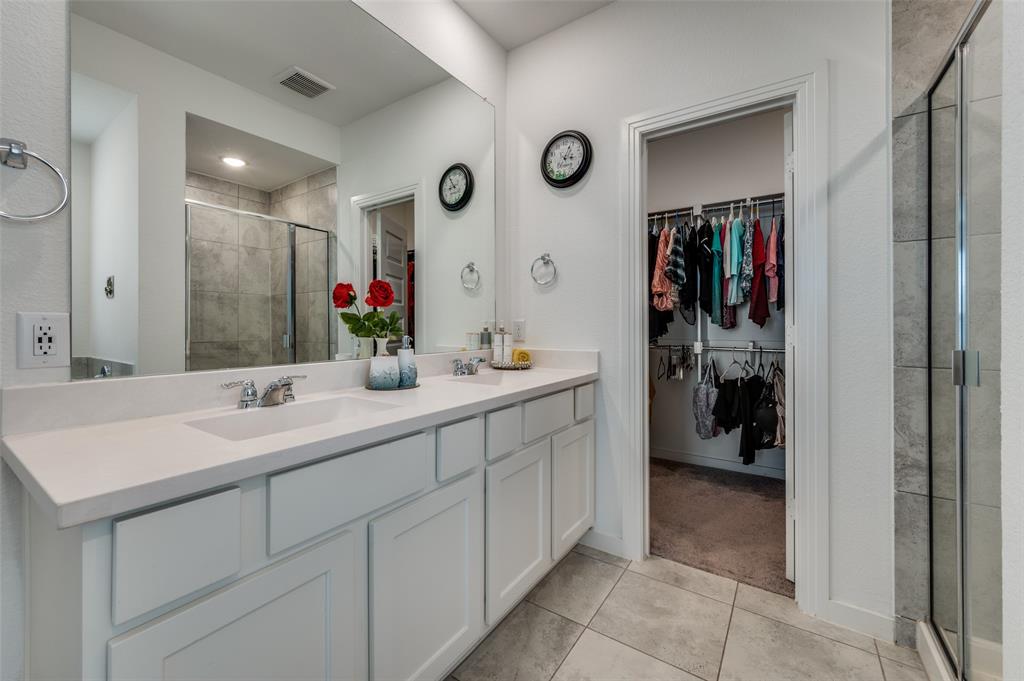 Bathroom with double vanity, a shower stall, light tile patterned floors, and a walk in closet