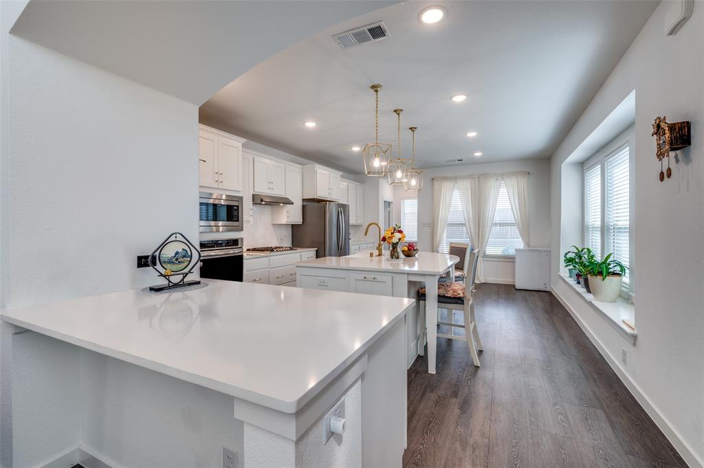 Kitchen featuring a breakfast bar, hanging light fixtures, white cabinetry, a center island with sink, and dark wood finished floors