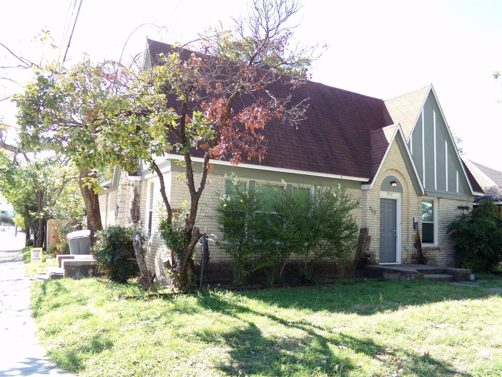 Tudor-style exterior featuring light-colored brick masonry, steeply pitched rooflines, prominent decorative timbering, an arched entryway, and a concrete front porch