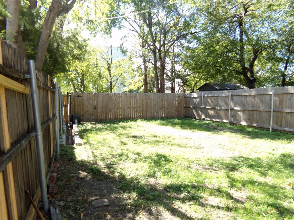 Backyard area featuring a wood fence, mature trees, and open lawn space