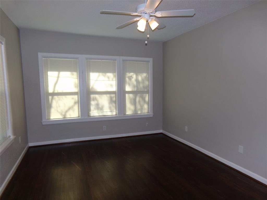 Room featuring wood-finish flooring, a neutral wall color palette, a triple-pane window configuration, and a ceiling-mounted light fixture with a multi-blade fan