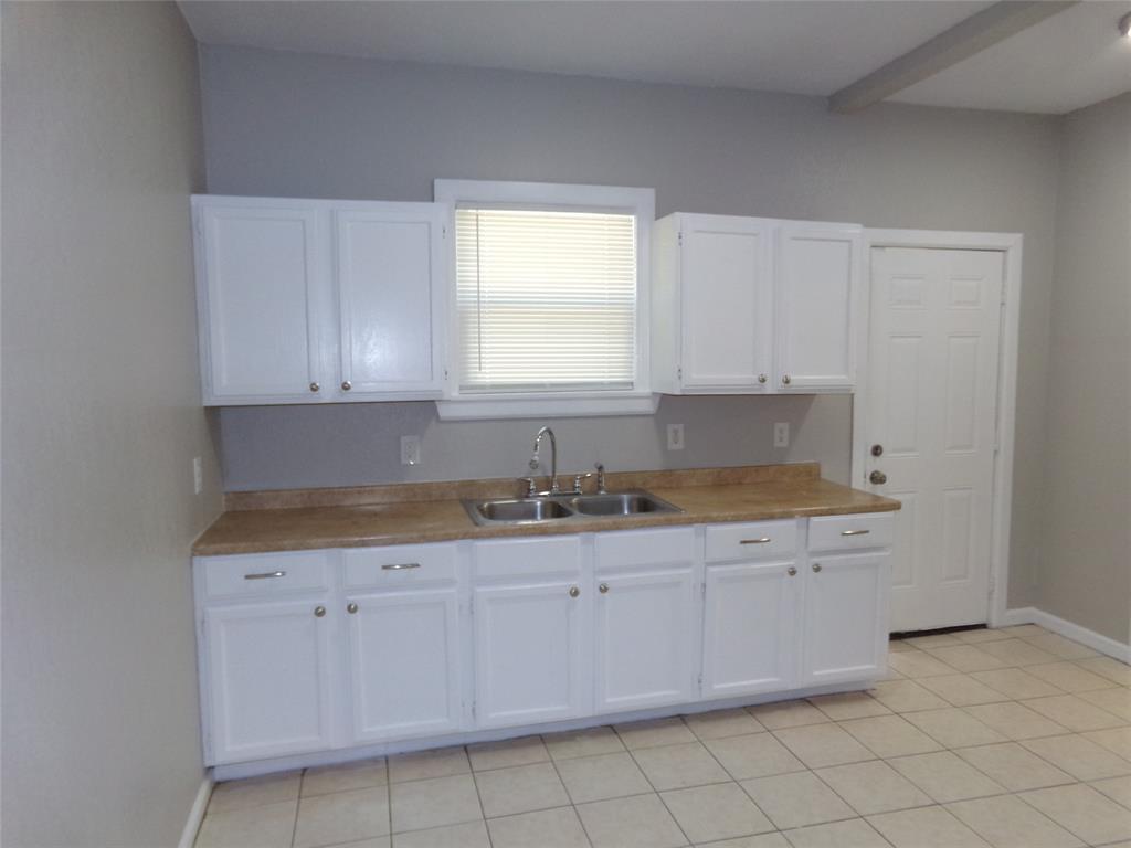 Kitchen featuring white shaker-style cabinetry, neutral-toned solid surface countertops, stainless steel dual-basin sink with arched faucet, and light ceramic tile flooring