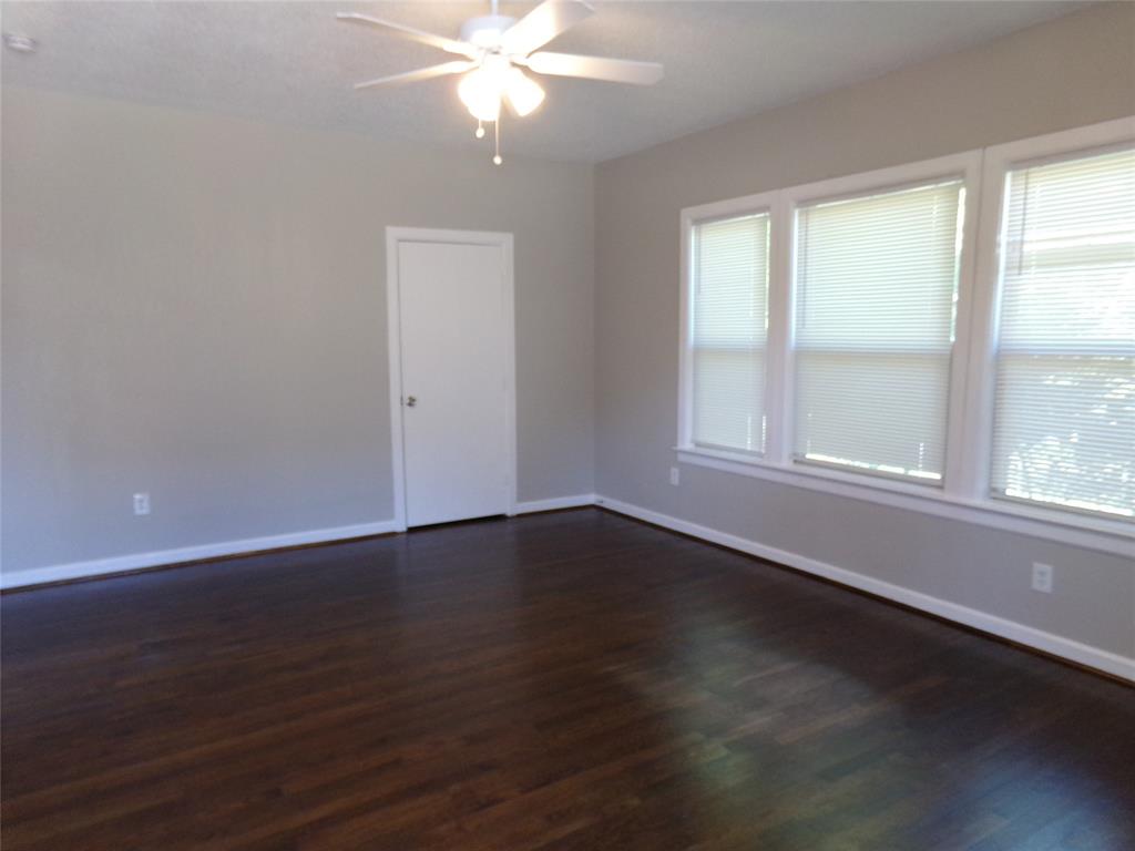 Neutral-toned interior space featuring dark wood-finish flooring, three large windows with horizontal blinds, and a central ceiling-mounted light fixture