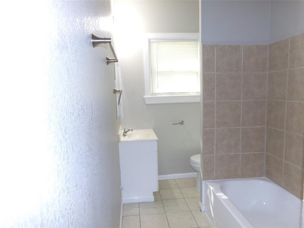 Bathroom featuring a neutral-tone tile tub surround, white pedestal vanity, ceramic tile flooring, and wall-mounted metal hardware