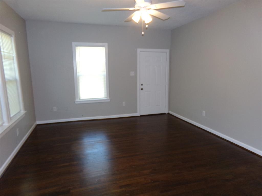 Interior room featuring wood-finish flooring, neutral wall paint, multi-pane windows, and a ceiling fan with integrated lighting