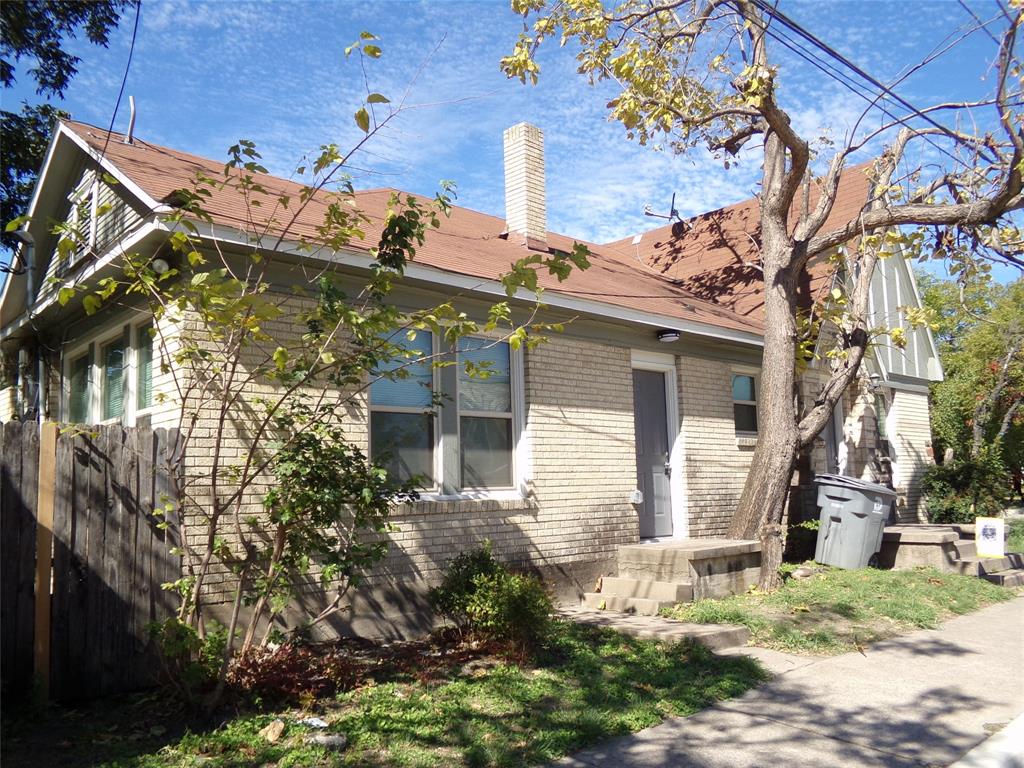 Exterior featuring light-colored brick siding, a gable roof with shingle finish, and a central masonry chimney