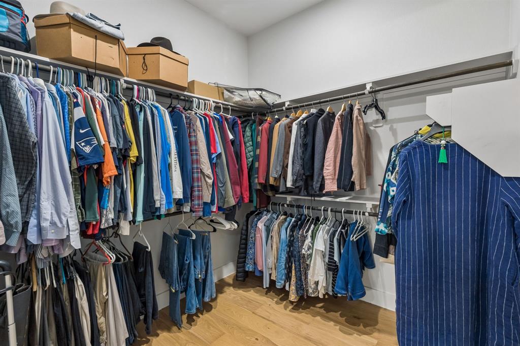 Walk-in closet featuring dual-level hanging rods, upper storage shelving, and wood-finish flooring
