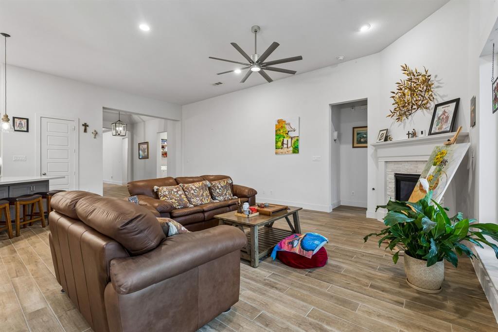 Living area featuring wood-finish flooring, vaulted ceilings, a multi-blade ceiling fan, recessed lighting, and a brick-surround fireplace with a mantel