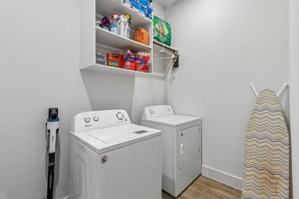 Laundry area featuring wood-finish flooring, white upper shelving, and a wall-mounted hanging rod Laundry area featuring wood-finish flooring, white upper shelving, and a wall-mounted hanging rod