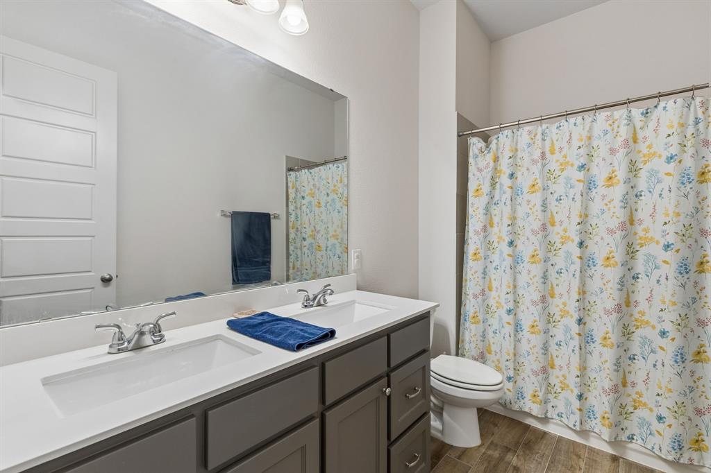 Double vanity featuring a white solid-surface countertop, dual drop-in sinks with polished chrome faucets, grey shaker-style cabinetry, and wood-finish flooring Double vanity featuring a white solid-surface countertop, dual drop-in sinks with polished chrome faucets, grey shaker-style cabinetry, and wood-finish flooring