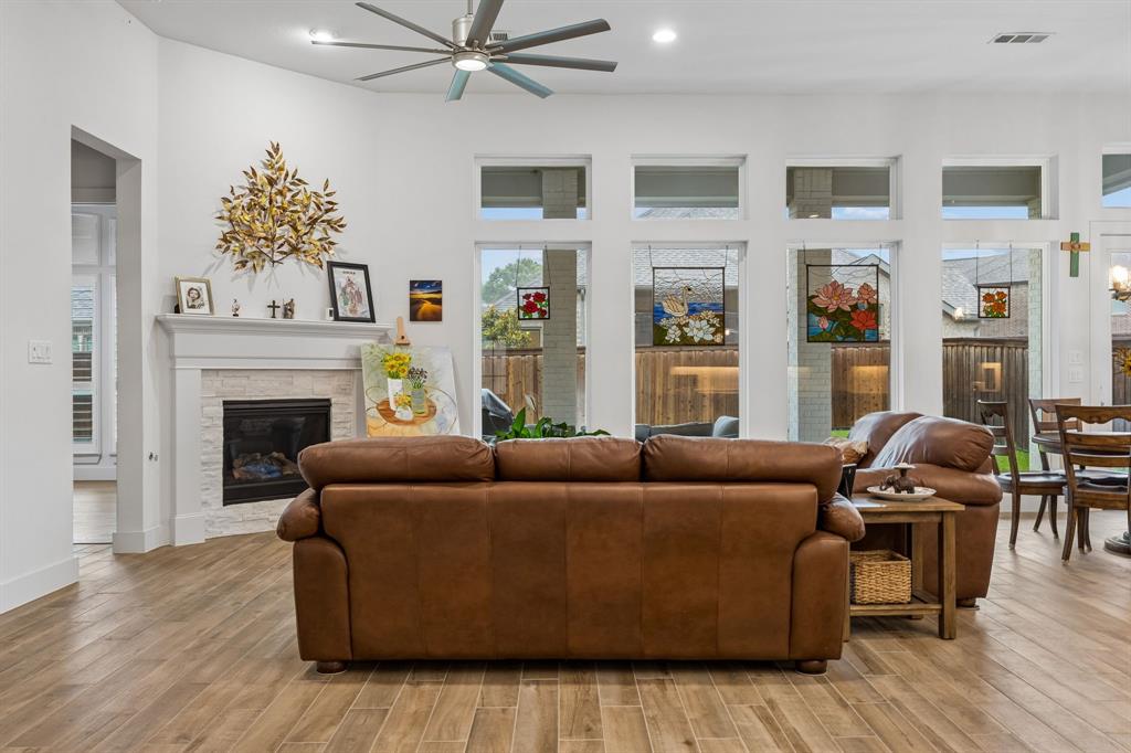Living area featuring wood-finish flooring, a white brick fireplace with a mantle, floor-to-ceiling windows with transoms, and a multi-blade ceiling fan