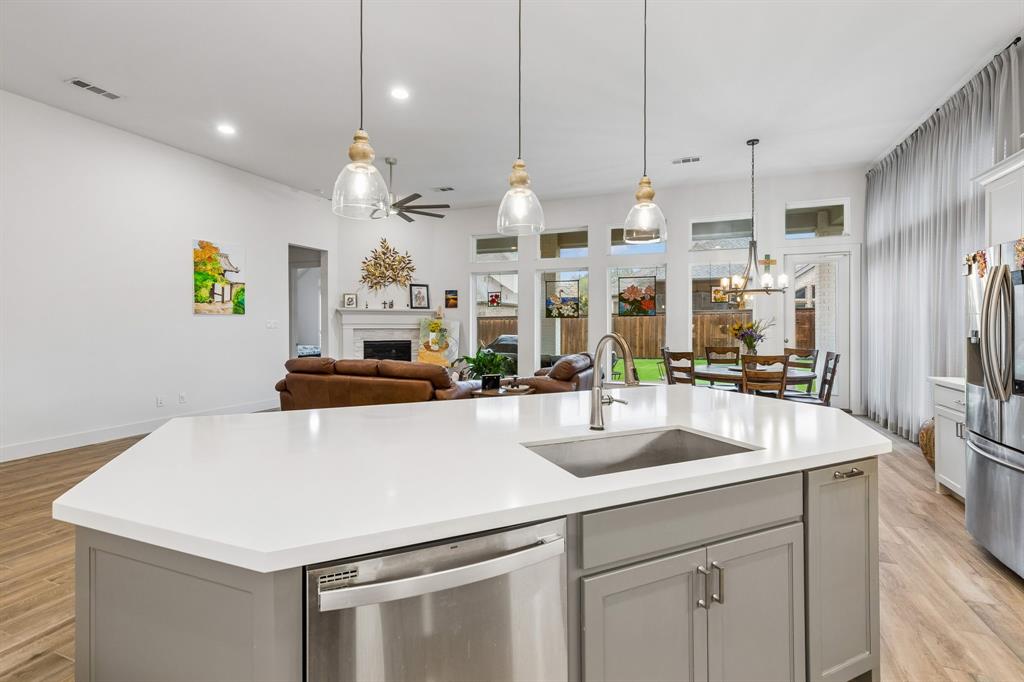 Kitchen island featuring a white countertop, undermount stainless steel sink, and gray cabinetry, illuminated by three pendant lights
