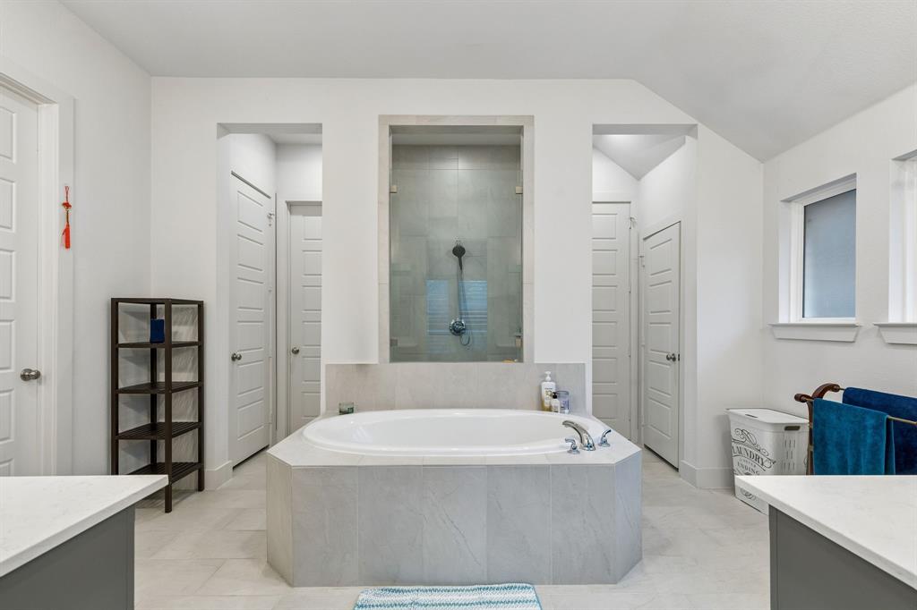 Bathroom featuring an oval soaking tub with a tiled surround, a glass-enclosed shower, dual vanity counters with stone-finish surfaces, and multiple panel doors