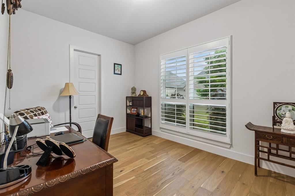 Interior room featuring wood-finish flooring, white walls, and large windows with integrated plantation-style shutters Interior room featuring wood-finish flooring, white walls, and large windows with integrated plantation-style shutters