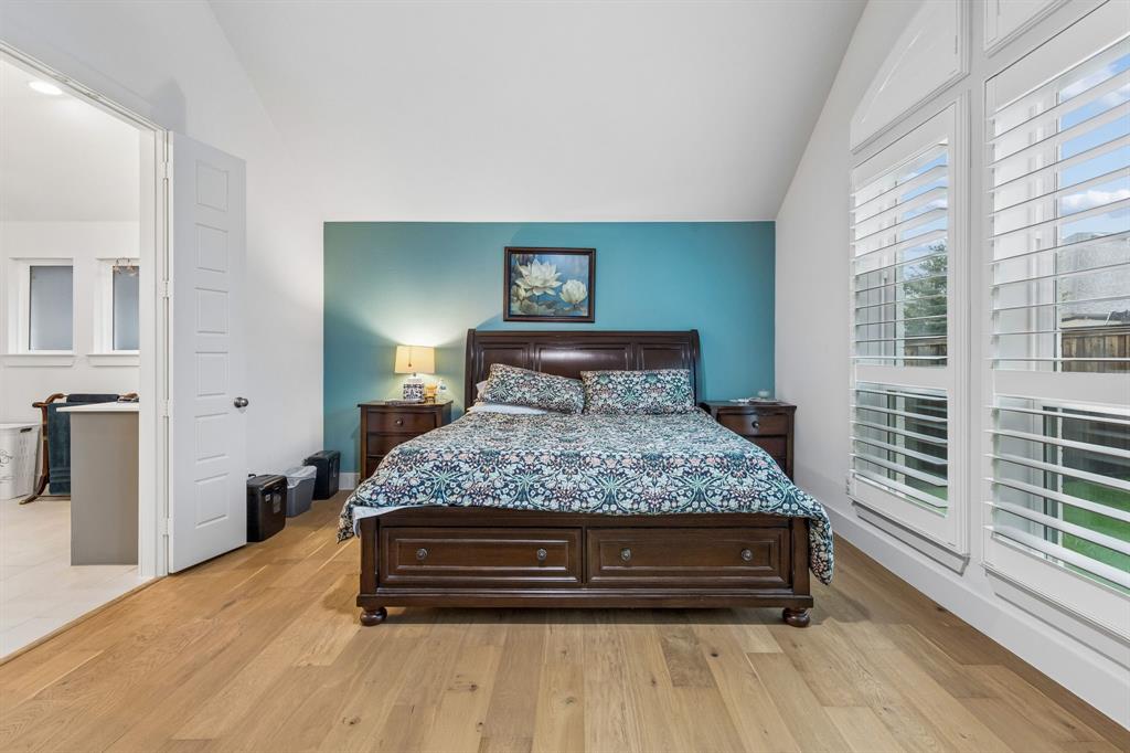 Vaulted ceiling, wood-finish flooring, accent wall, and multi-pane windows with fitted shutters