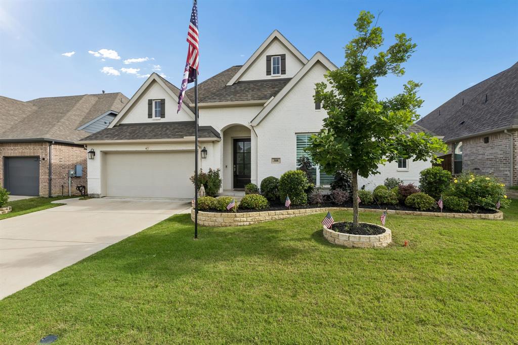 Brick exterior residence featuring a multi-gabled roofline, concrete driveway, attached two-car garage, and tiered stone garden beds Brick exterior residence featuring a multi-gabled roofline, concrete driveway, attached two-car garage, and tiered stone garden beds