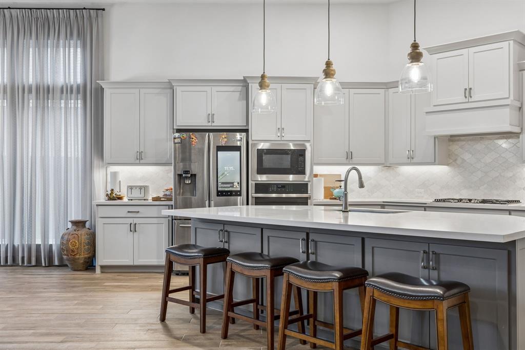 Kitchen featuring a central island with a quartz countertop, custom cabinetry, stainless steel built-in appliances, pendant lighting, and wood-finish flooring