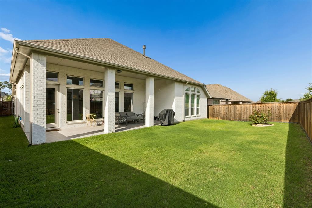 Rear exterior featuring white painted brick masonry, a covered concrete patio, and a fenced backyard with a lawn