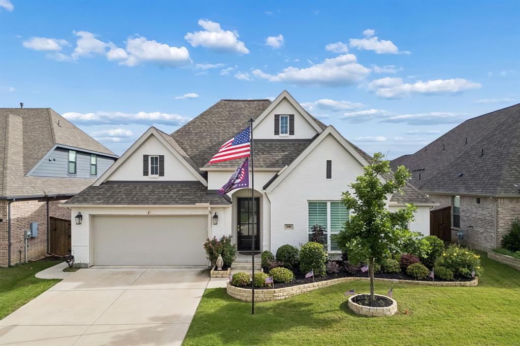 Painted brick exterior featuring a multi-gabled roofline, two-car garage, and stone-bordered landscaping beds with established shrubbery