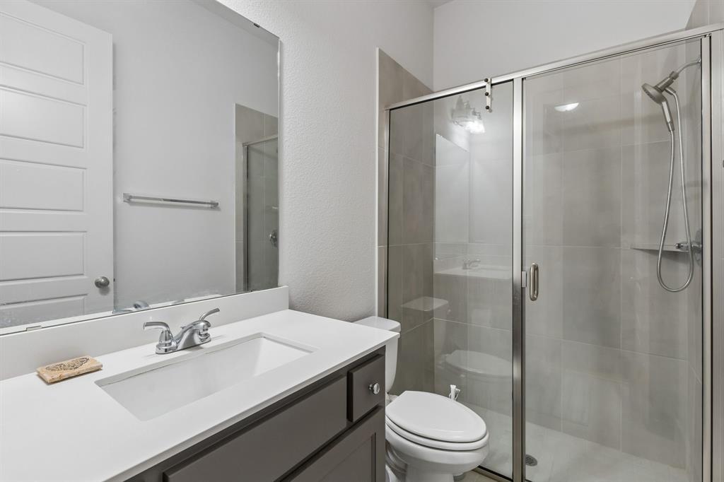 Bathroom featuring a vanity with a white countertop and rectangular undermount sink, large wall-mounted mirror, and walk-in shower with tiled surround and glass sliding enclosure